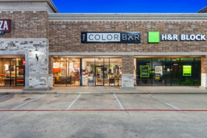 - The Color Bar, TX A brick strip mall with storefronts for The Color Bar Hair Salon and H&R Block, featuring large glass windows and empty parking spaces in front. - The Color Bar, TX