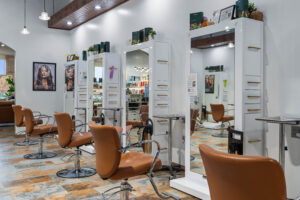 - The Color Bar, TX A modern hair salon with brown chairs, large mirrors, white cabinets, and shelves displaying hair products. The space is brightly lit, features posters on the wall, and offers trendy services like balayage and precise haircuts. - The Color Bar, TX