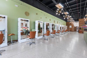 - The Color Bar, TX Modern hair salon interior with green walls, multiple styling stations for your next haircut or hair color, brown chairs, mirrors, and bright lighting fixtures. The salon appears clean and organized. - The Color Bar, TX