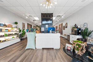 - The Color Bar, TX Modern salon interior with white reception desk, product shelves on the left, decorative plants, wall art, and a light wood floor—perfect for your next balayage or hair highlights by a skilled hair stylist. - The Color Bar, TX