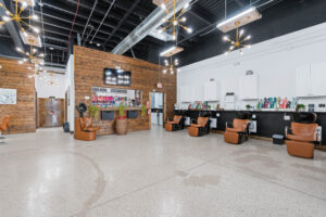 - The Color Bar, TX Modern hair salon interior with brown leather chairs, wash basins, wooden accents, and shelves of hair products—perfect for your next haircut or hair color—set against white walls under exposed ceilings and pendant lights. - The Color Bar, TX