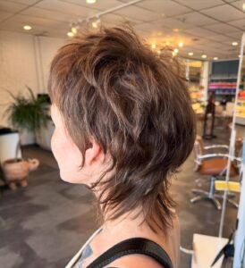 - The Color Bar, TX Person with a layered, textured mullet hairstyle and subtle hair highlights in a modern hair salon, viewed from the side. - The Color Bar, TX