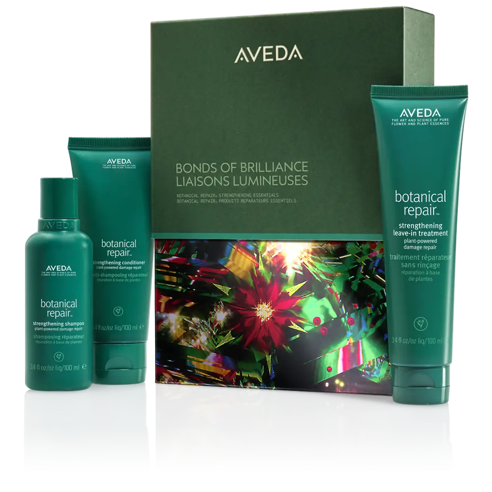 - The Color Bar, TX Aveda Bonds of Brilliance botanical repair gift set with three green bottles—shampoo, conditioner, and leave-in treatment—shown in front of a colorful box for radiant hair and winter hair rituals. - The Color Bar, TX