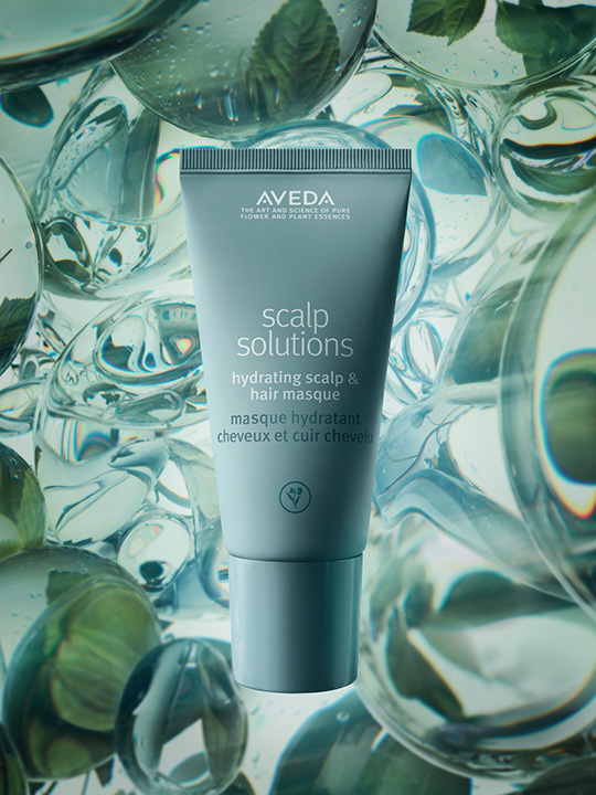 - The Color Bar, TX A tube of Aveda Scalp Solutions Hydrating Scalp & Hair Masque, perfect for scalp care, is displayed against a background of clear and green liquid bubbles with mint leaves. - The Color Bar, TX