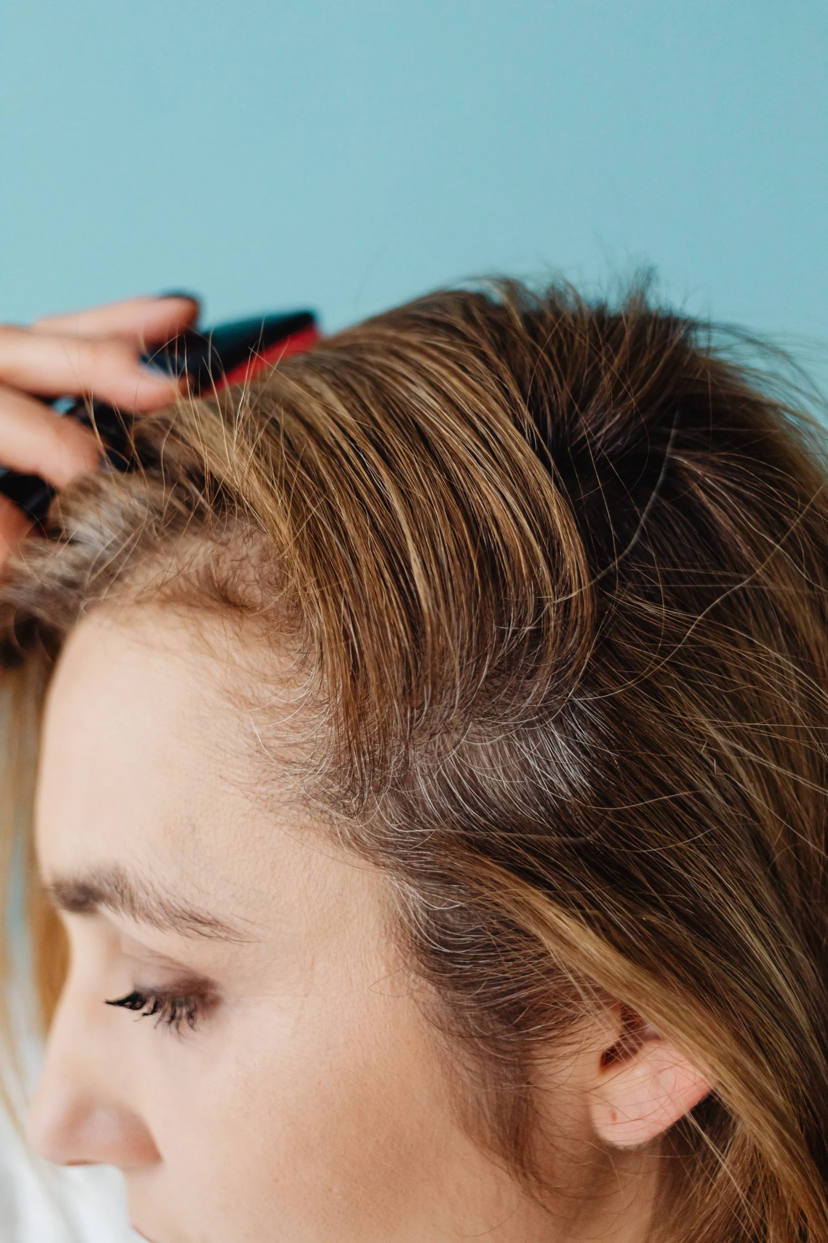 - The Color Bar, TX A person using a comb on their hair, revealing grey roots at the part that may benefit from hair loss solutions in Texas. - The Color Bar, TX